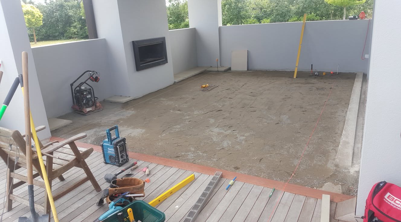 Outdoor construction in progress: a timber deck and paved patio being built against a new build